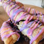 Three Cheshire Cat Tail Pastries stacked on top of each other, they are puff pastries with purple and pink icing.