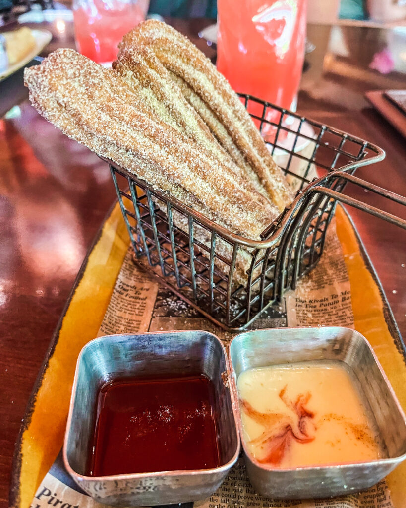 Churros in a basket with two dipping sauces in front, a chili-strawberry and a Vanilla Crema